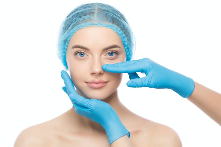 Young woman prepares for rhinoplasty while doctor in blue gloves touches her nose